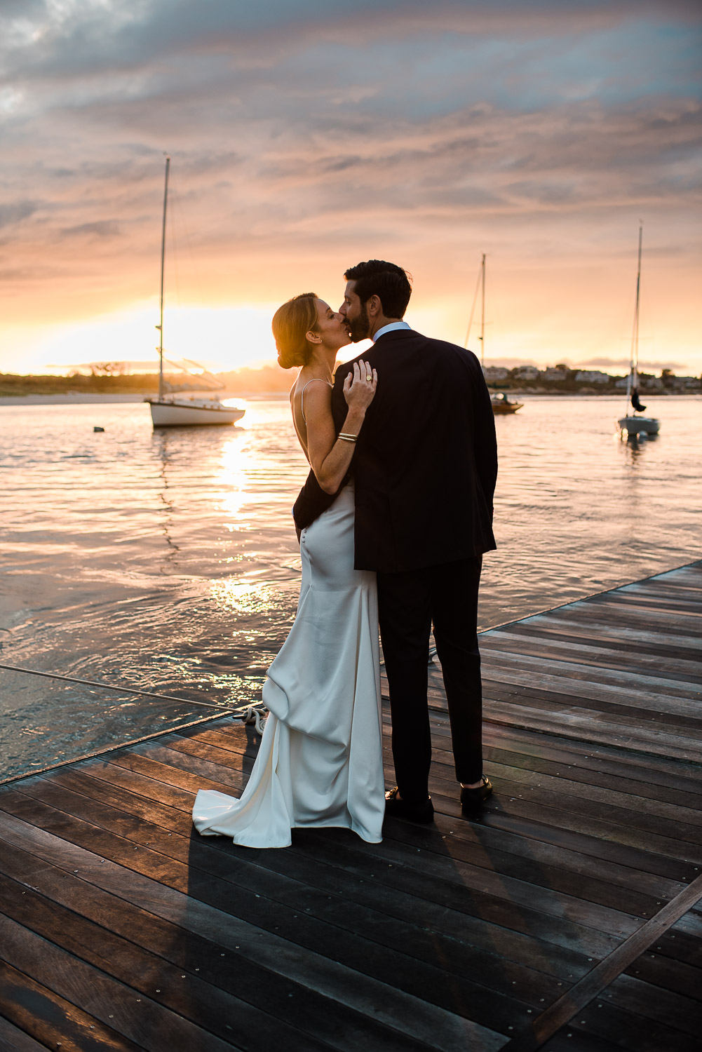 bride and groom from behind kissing at sunset on a dock at the Annisquam Yacht Club