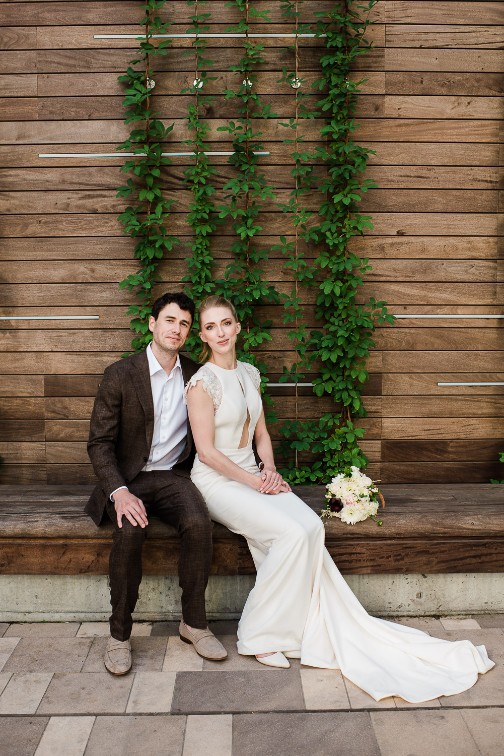 bride and groom sitting on bench in front of ivy and wood wall at the Boston Commonwealth Restaurant