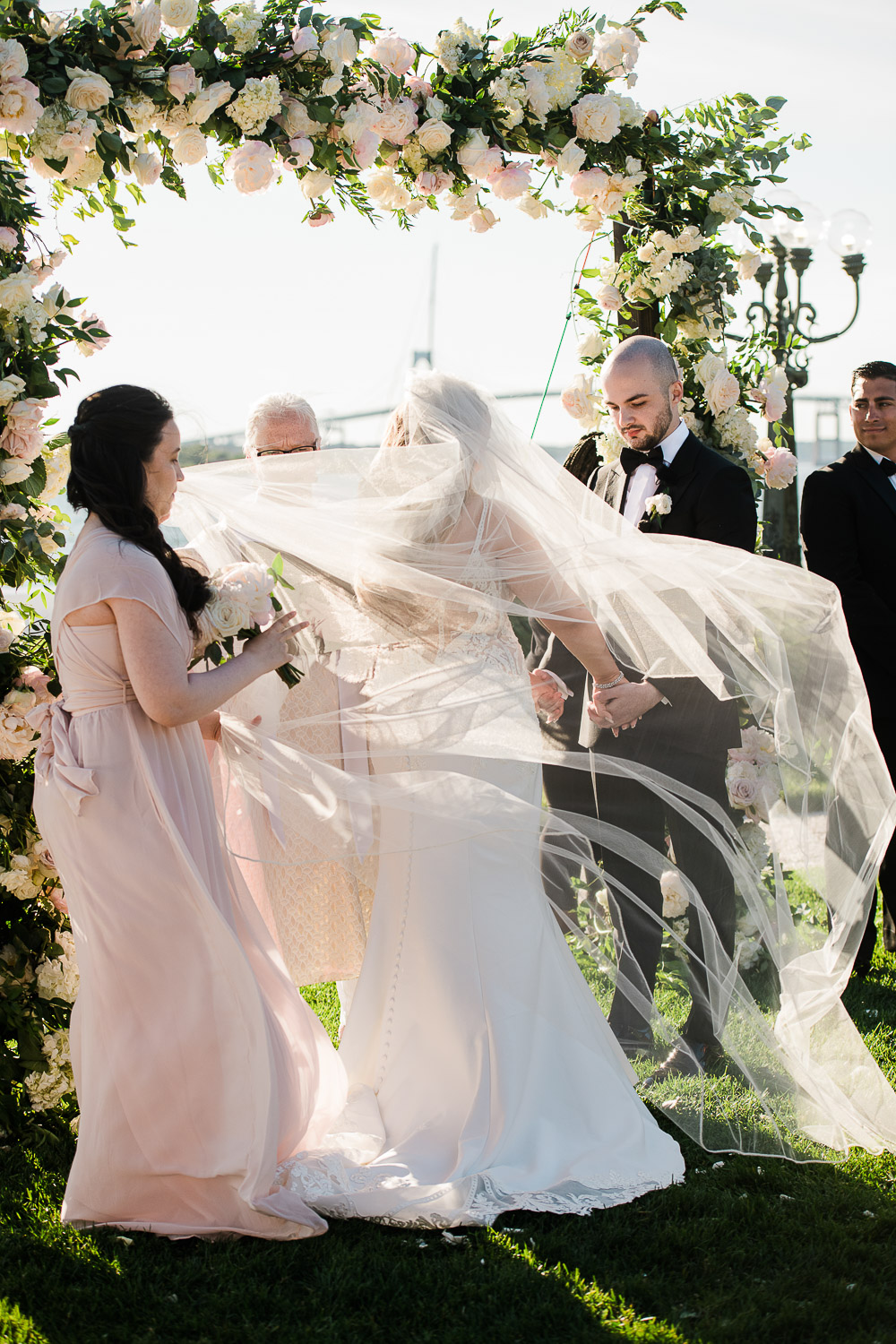 bride and groom under floral ceremony arbor with windblown veil at Belle Mer in Newport