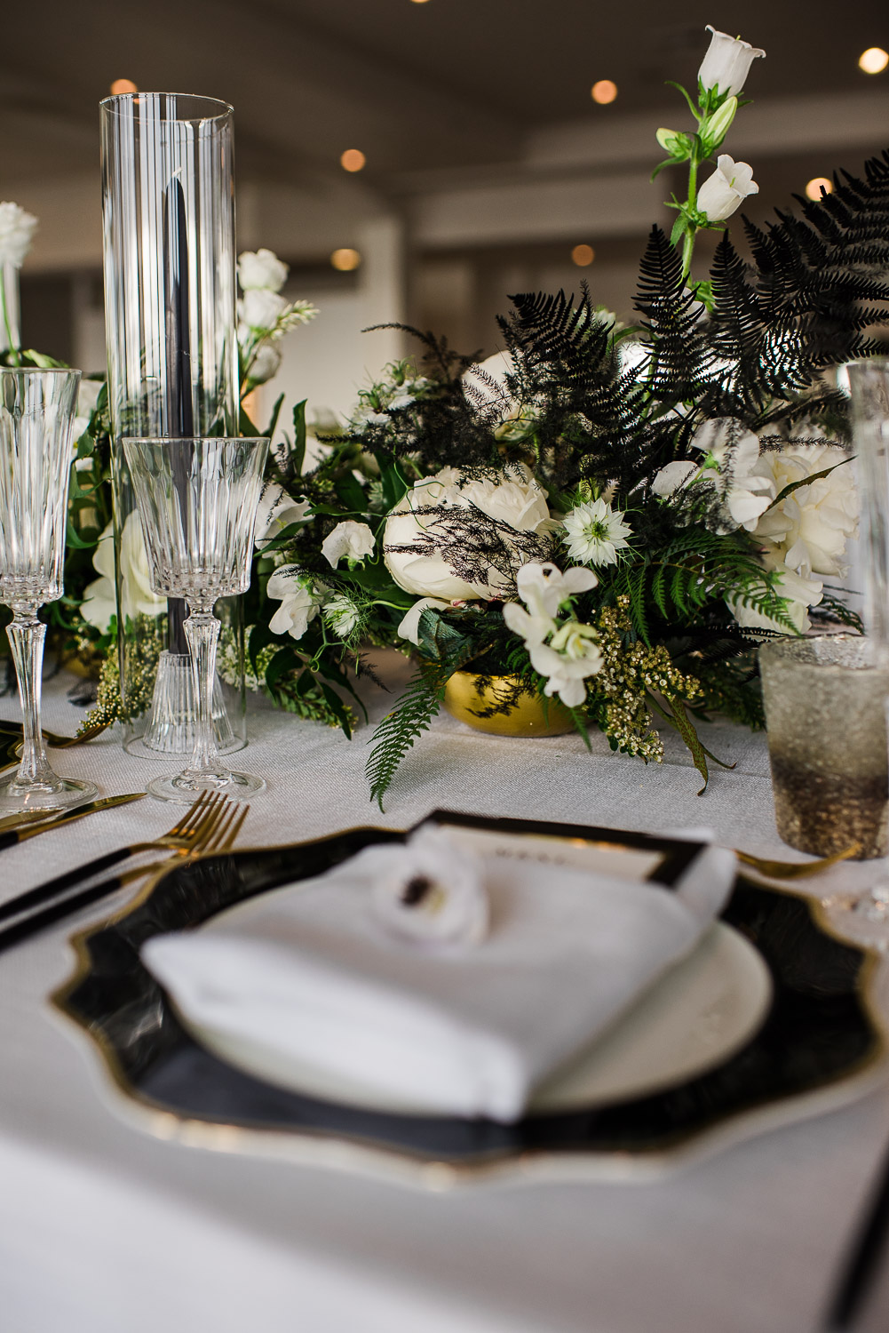 black white and green floral wedding table centerpiece with black and gold trimmed plates and white linen napkins