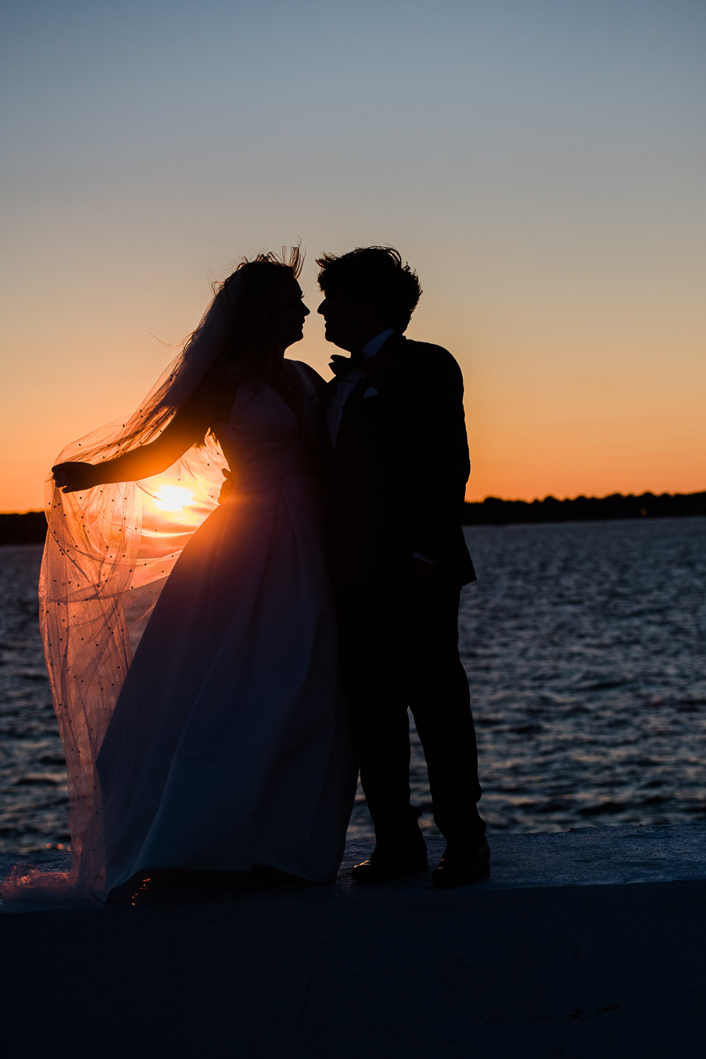 bride and groom orange sunset silhouette in front of water at Belle Mer in Newport RI