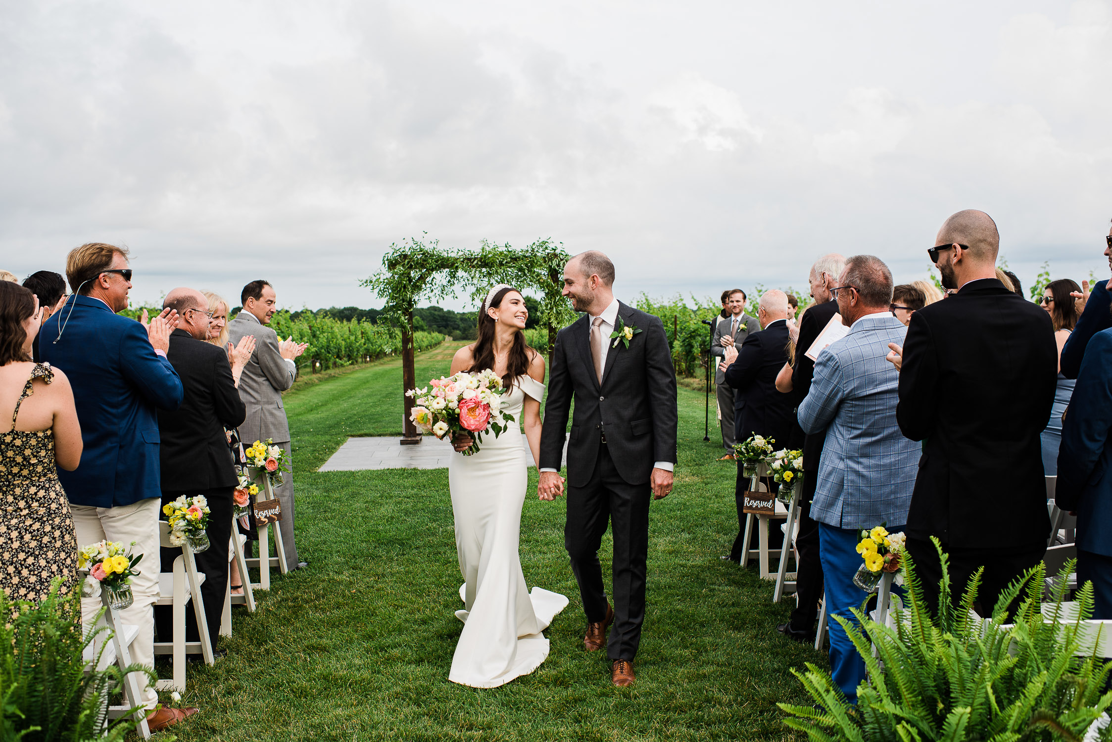 bride and groom looking at each other walking down ceremony aisle at the Saltwater Farm Vineyard