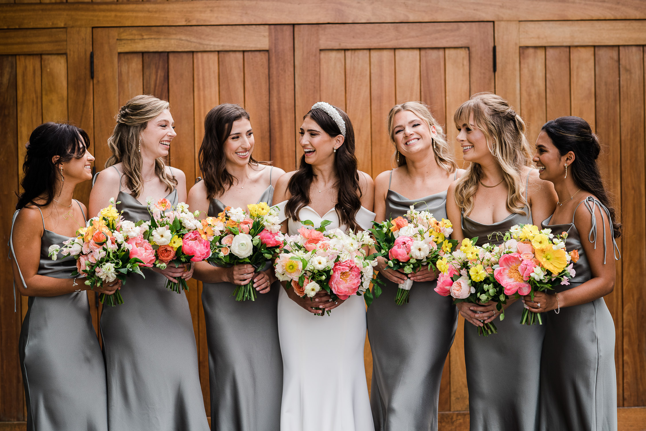 bride and bridesmaids laughing in front of wooden door at the Saltwater Farm Vineyard