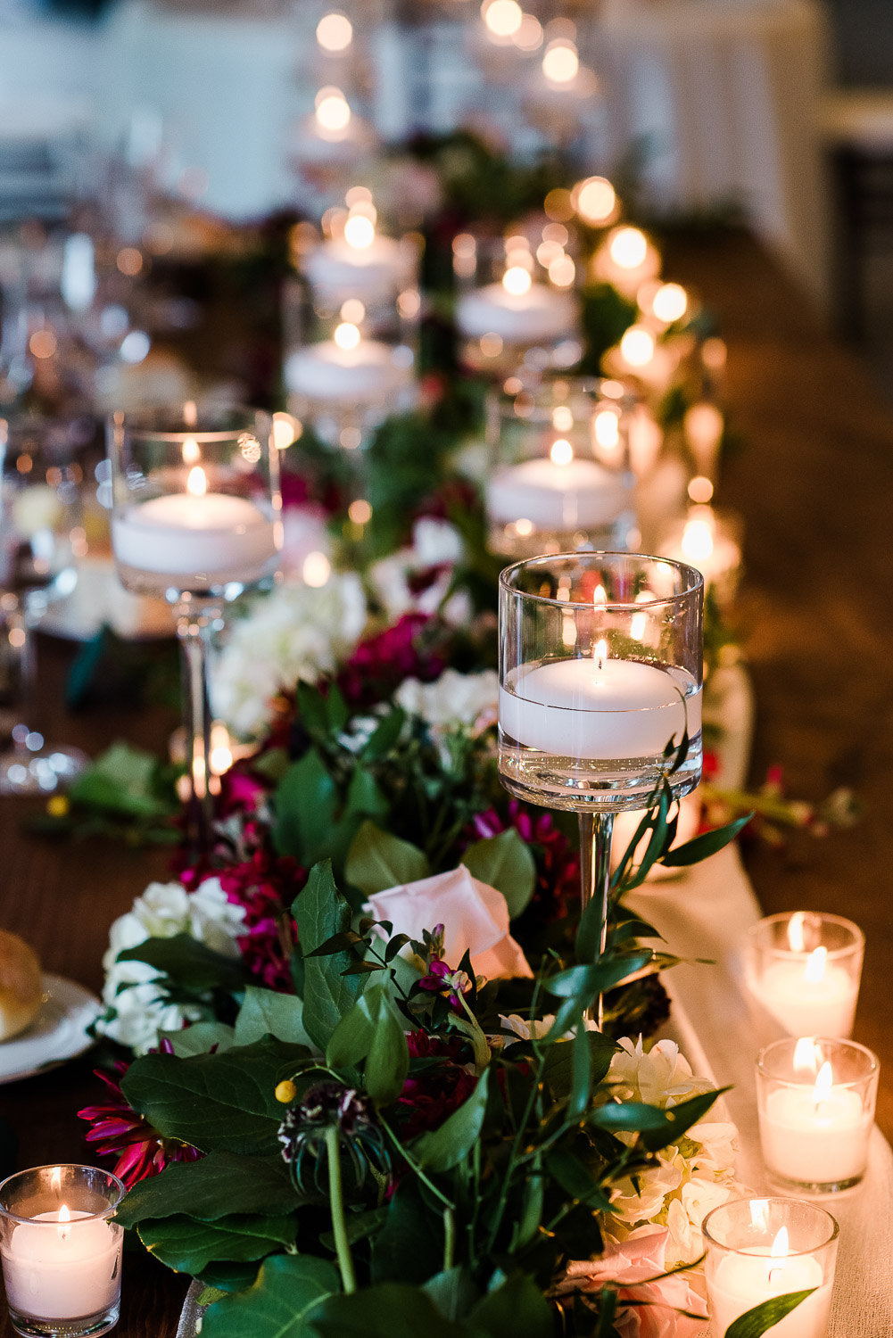 wedding table centerpiece with lit candles and red and pink florals and greenery