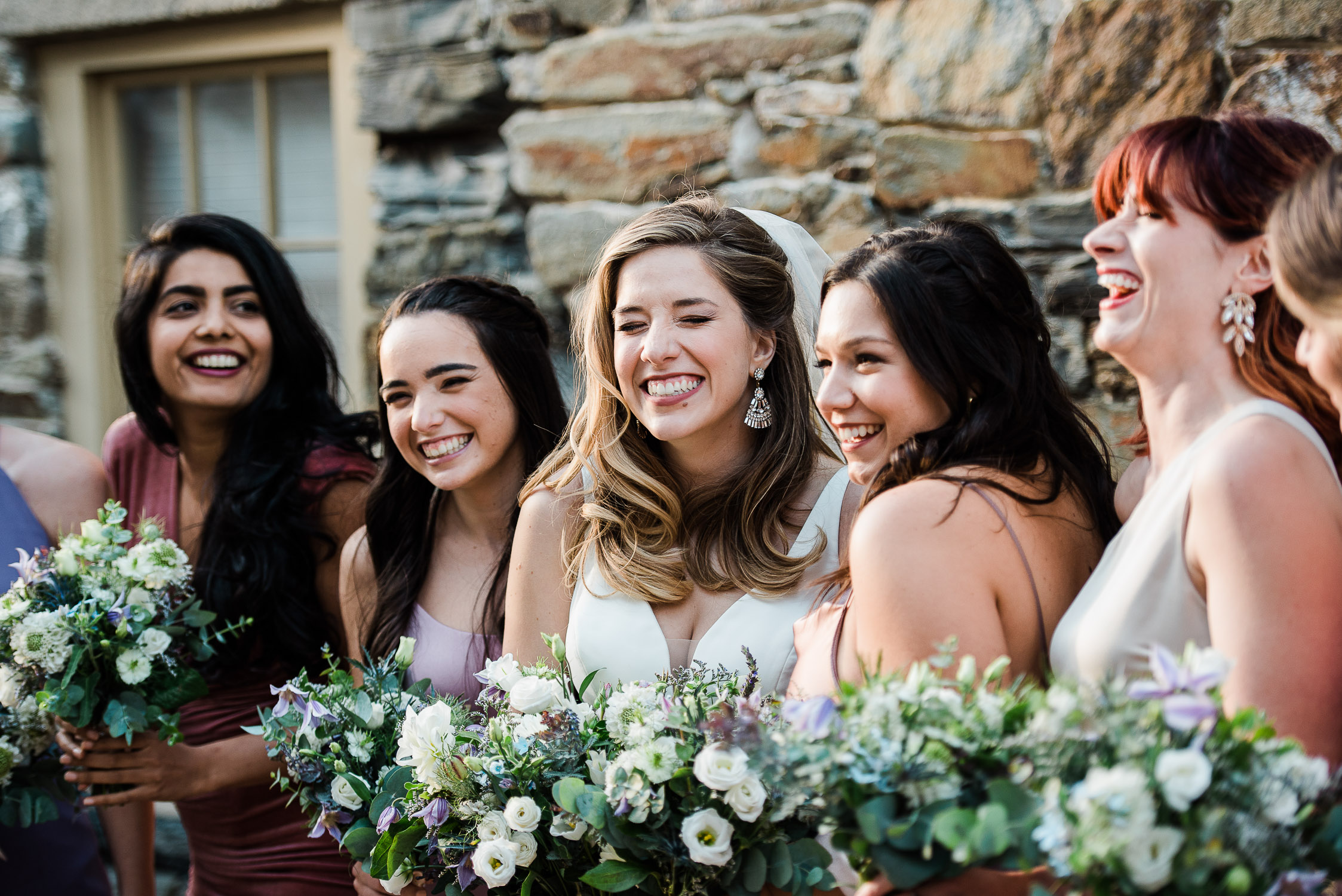 bride and bridesmaids laughing in front of stone wall at the Bristol Harbor Inn