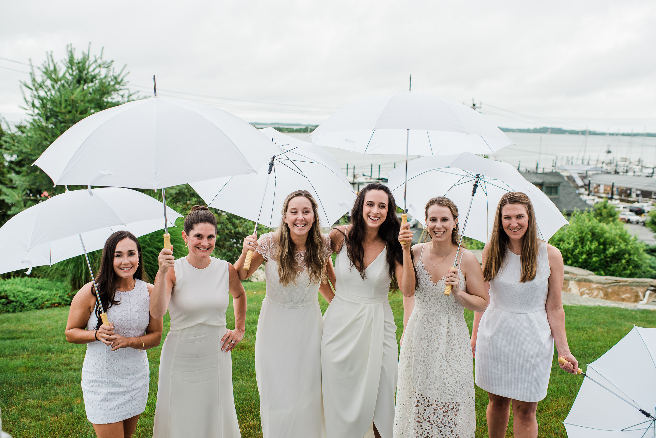 bride and bridesmaid in white dresses holding white umbrellas in Noank Ct