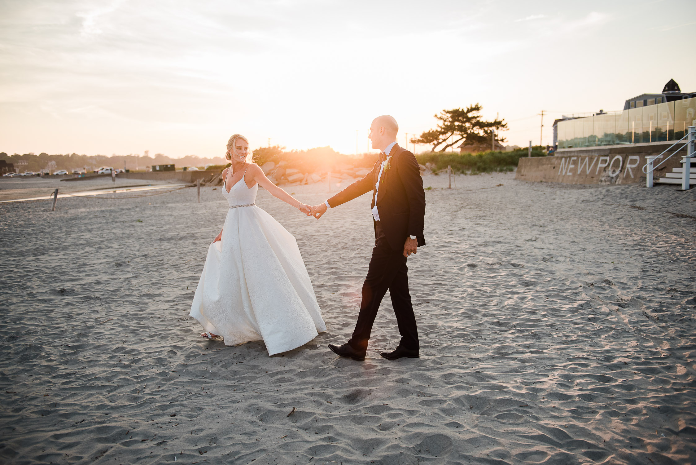 bride and groom holding hands and walking on the beach at sunset at the Newport Beach House