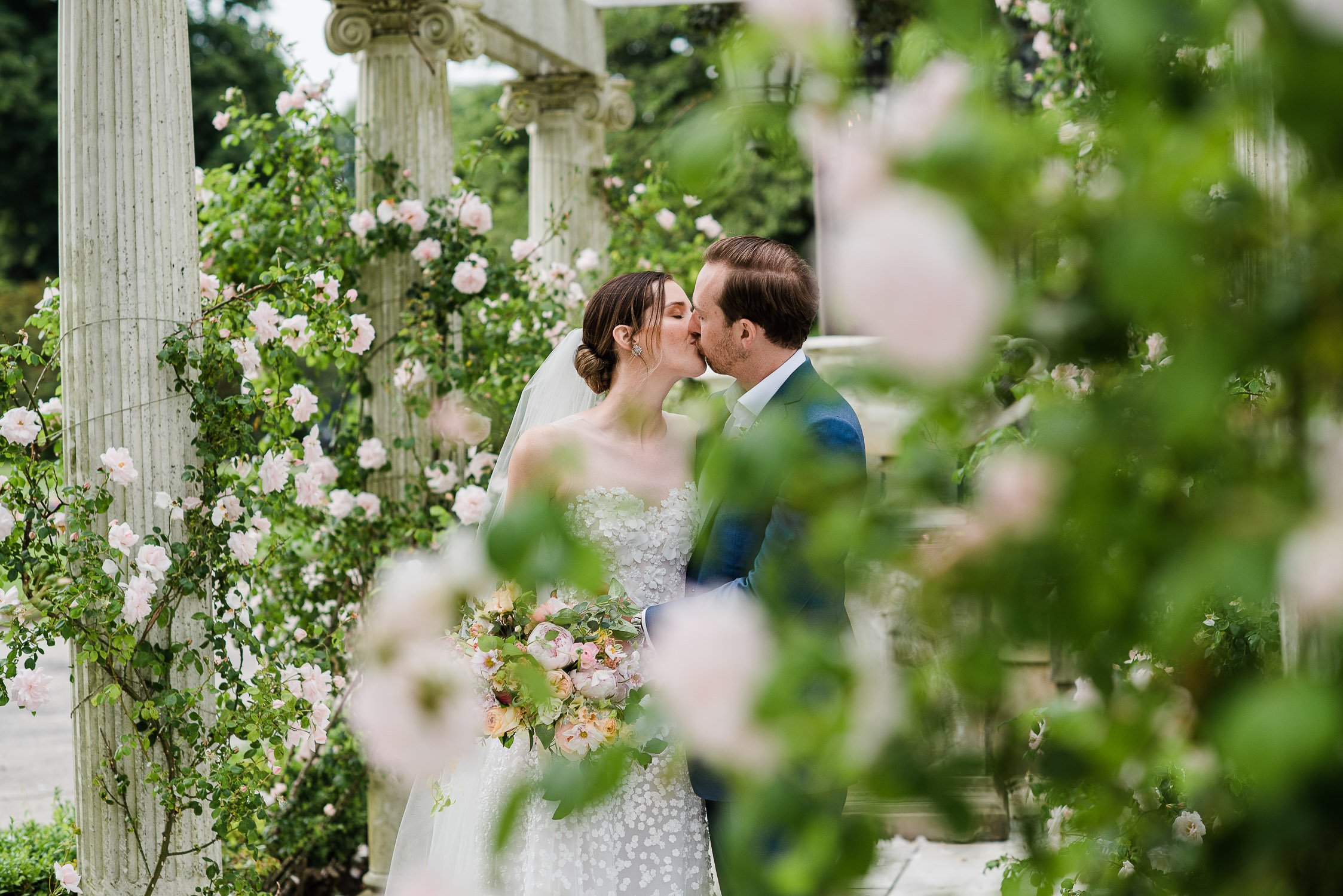 bride and groom kissing under floral columns
