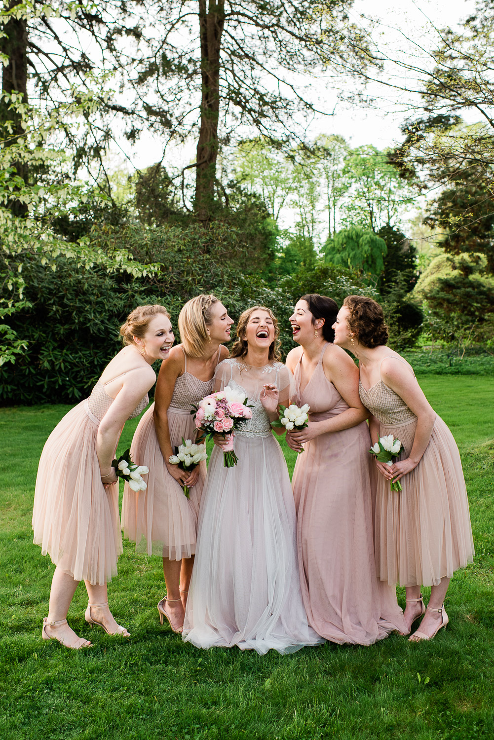 bride and bridesmaids laughing on lawn at Blithewold Mansion