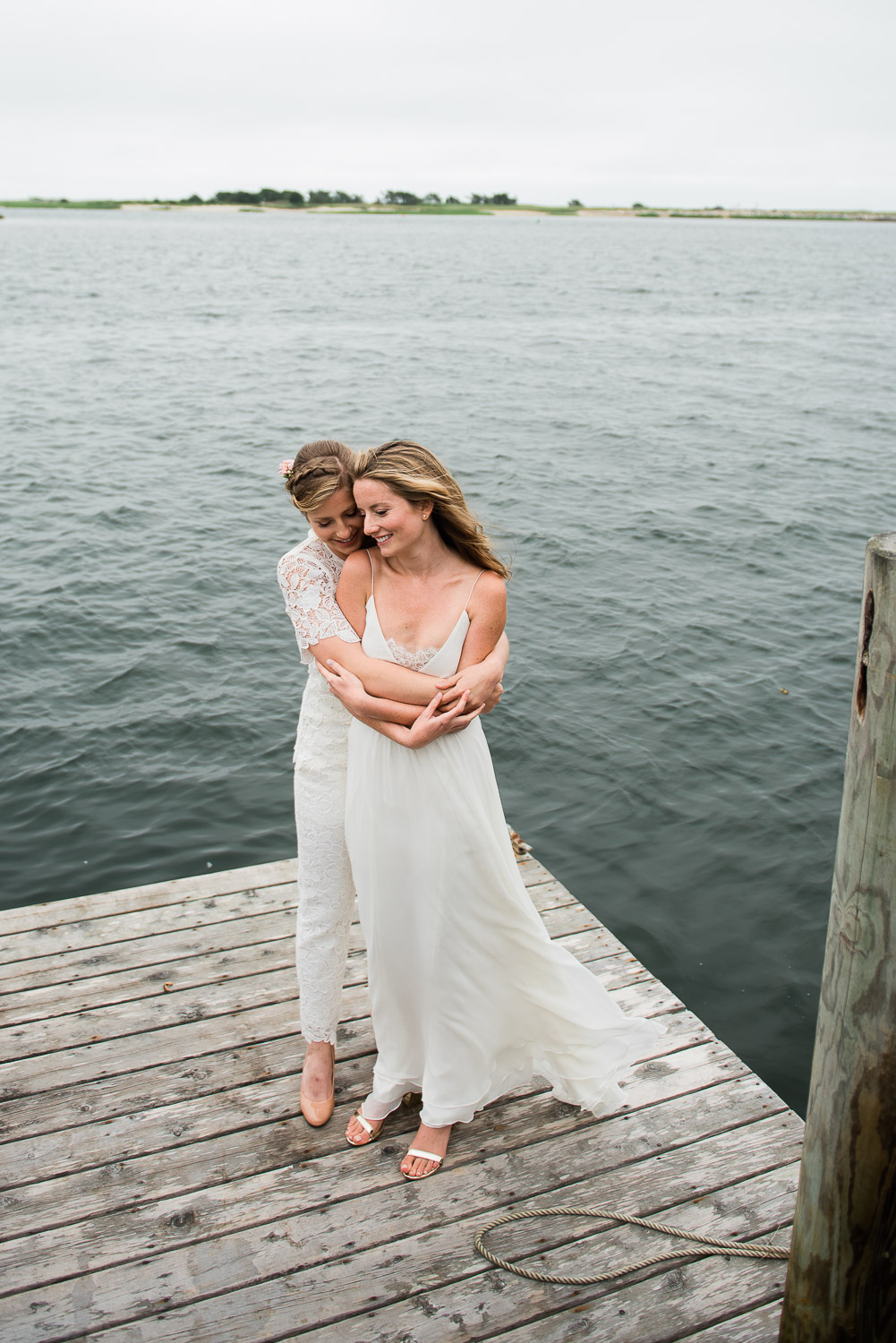 brides embracing on a dock in front of the water on Cape Cod