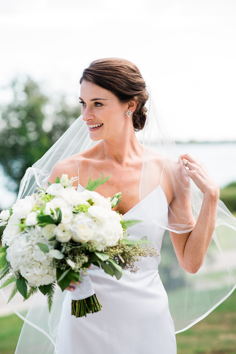 bride with white and green bouquet touching veil in Westerly RI