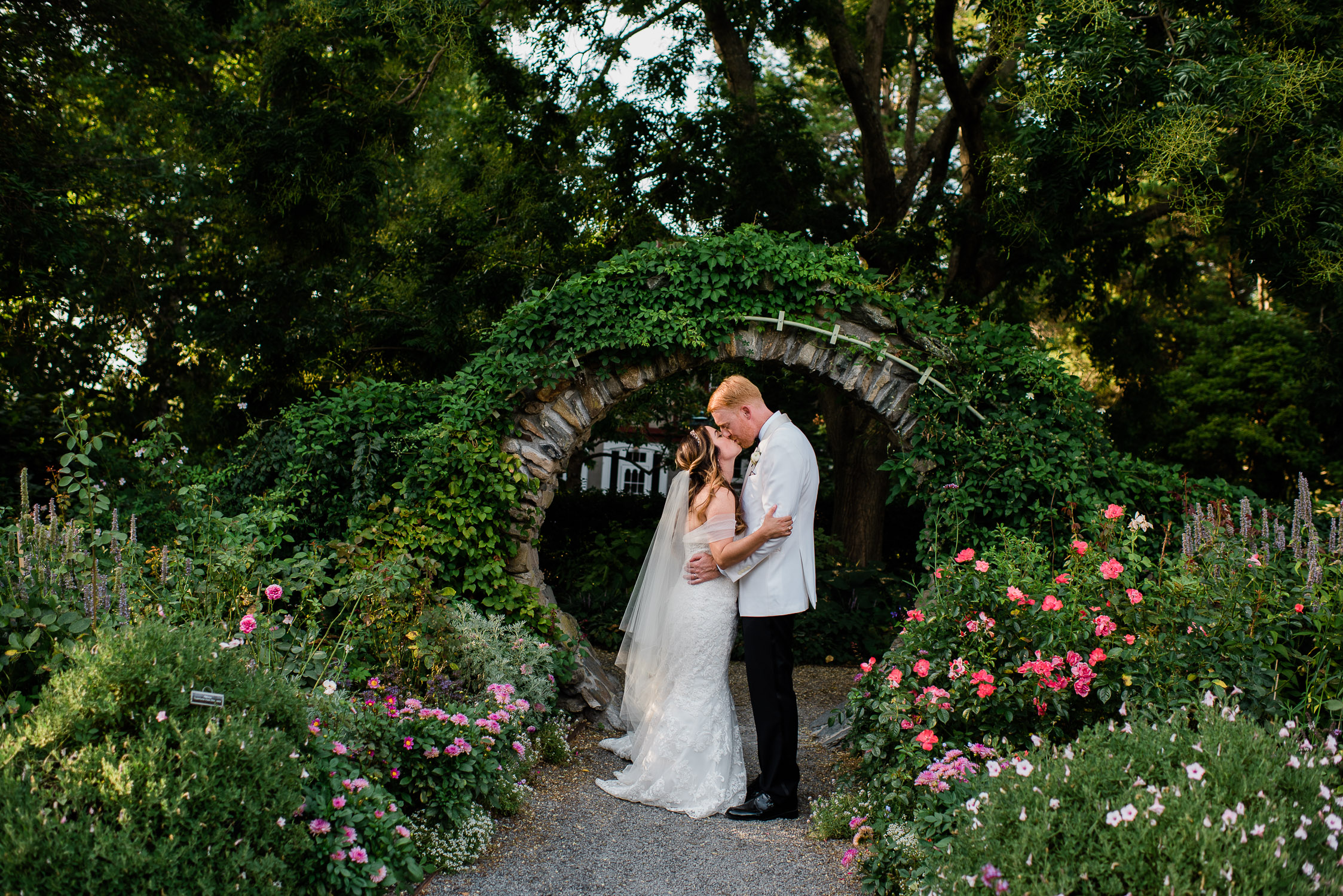 bride and groom kissing in front of stone and greenery arch at Blithewold Mansion