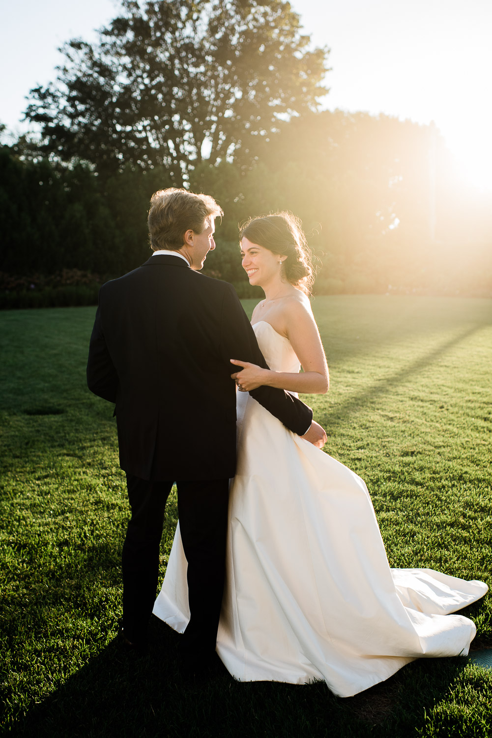 bride and groon facing each other in sun flare on the lawn of the Ocean House