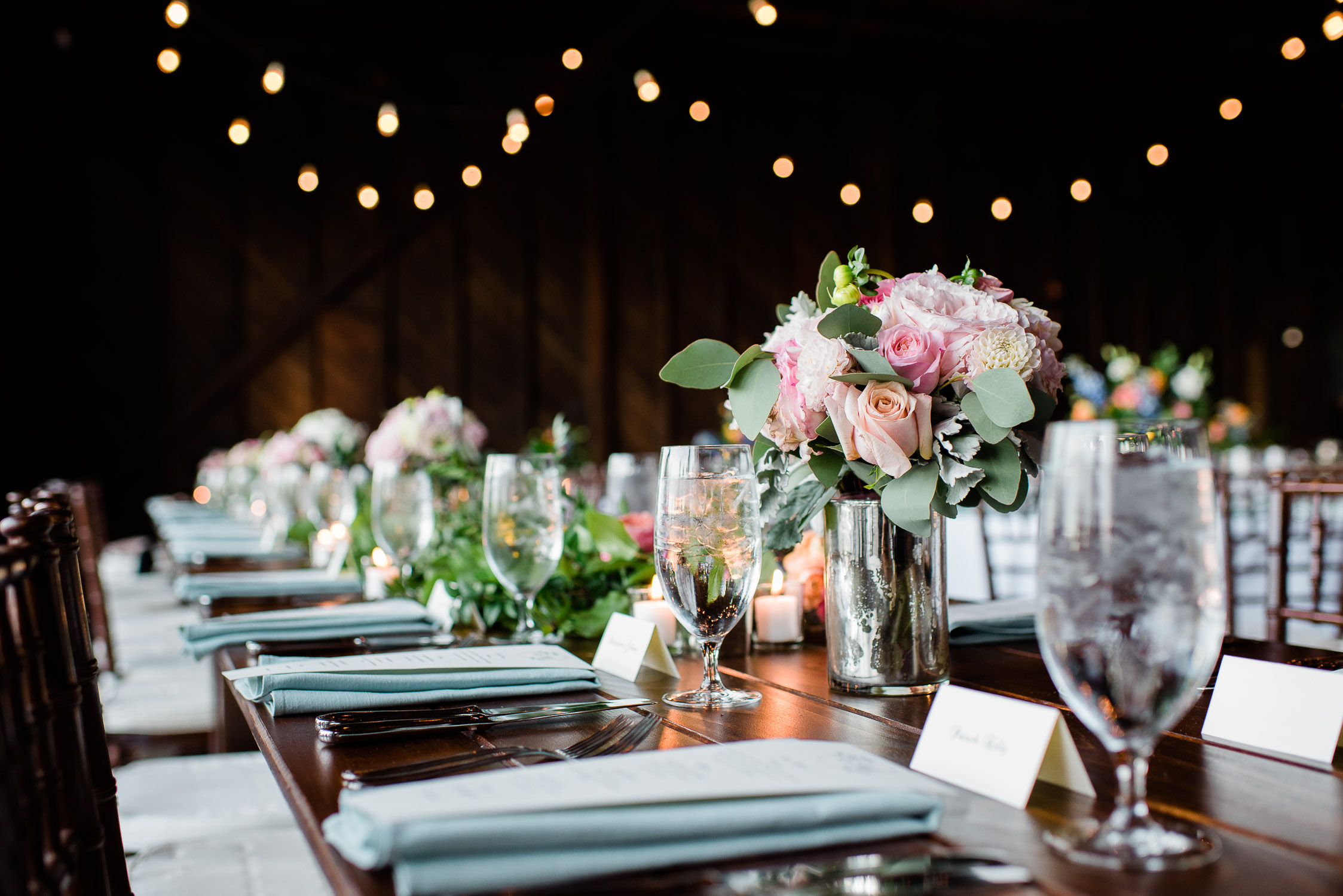 dark wood table with blue linens and pink and peach and white floral wedding centerpieces at the Saltwater Farm Vineyard