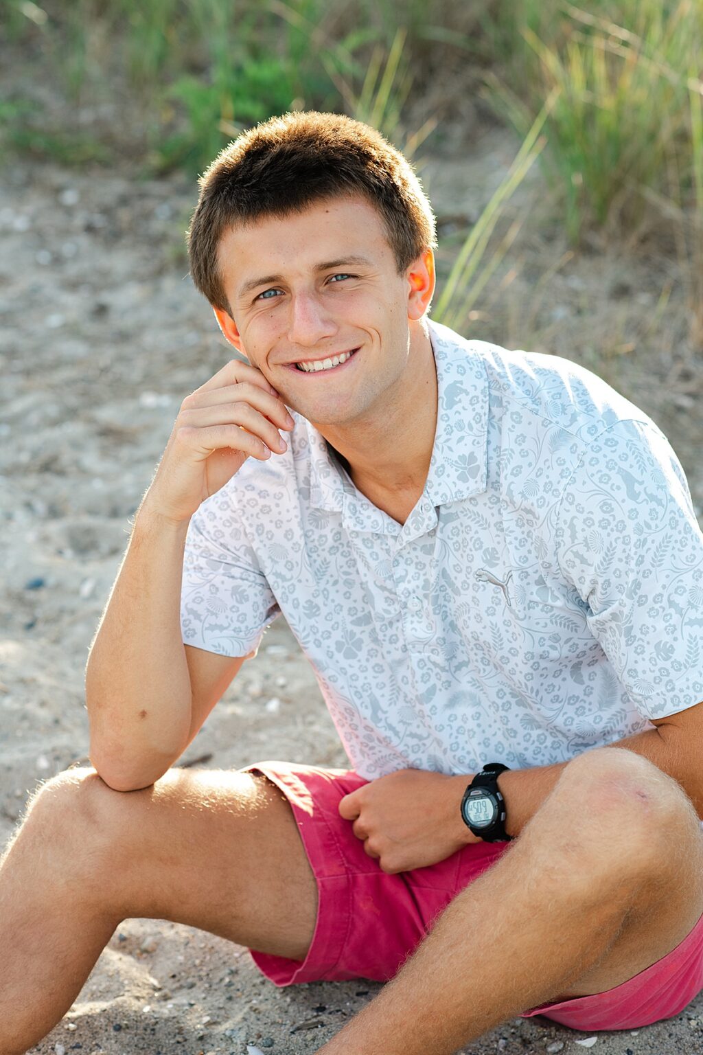 Senior boy sitting on sand at beach in front of tall grass