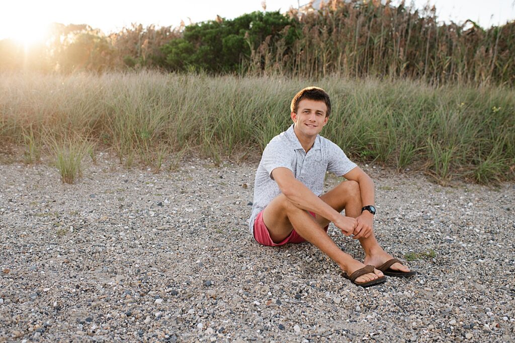 Portrait of senior boy sitting on beach with sunlight in background