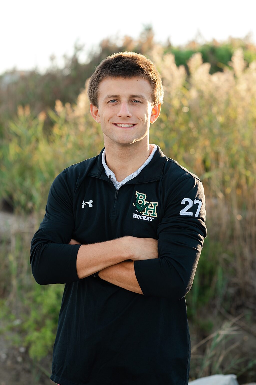 Senior boy in backlit sunset standing in front of tall grass
