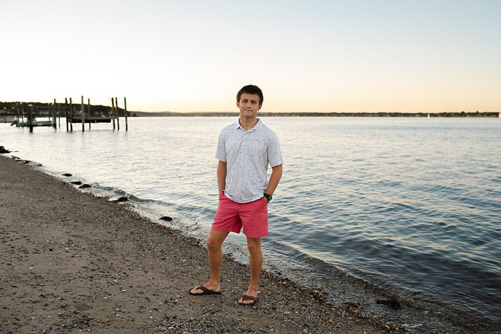 Sandy point senior session of boy standing on beach in front of water