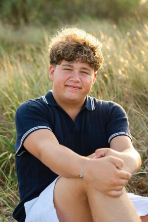 Senior portrait at Sandy Point Beach in Warwick, Rhode Island during golden hour, with tall coastal grass and warm sunlight.