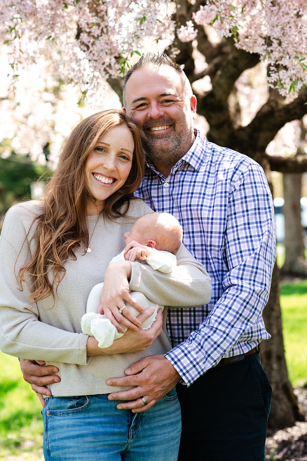 parents portrait with their newborn baby in front of pink blossoming tree