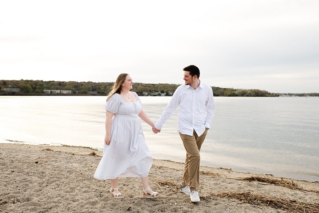 engaged couple walking hand in hand on the beach