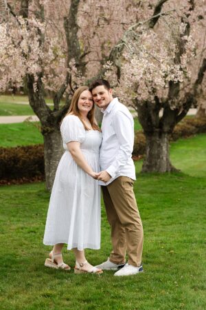 engaged couple holding hands in front of blossoming tree