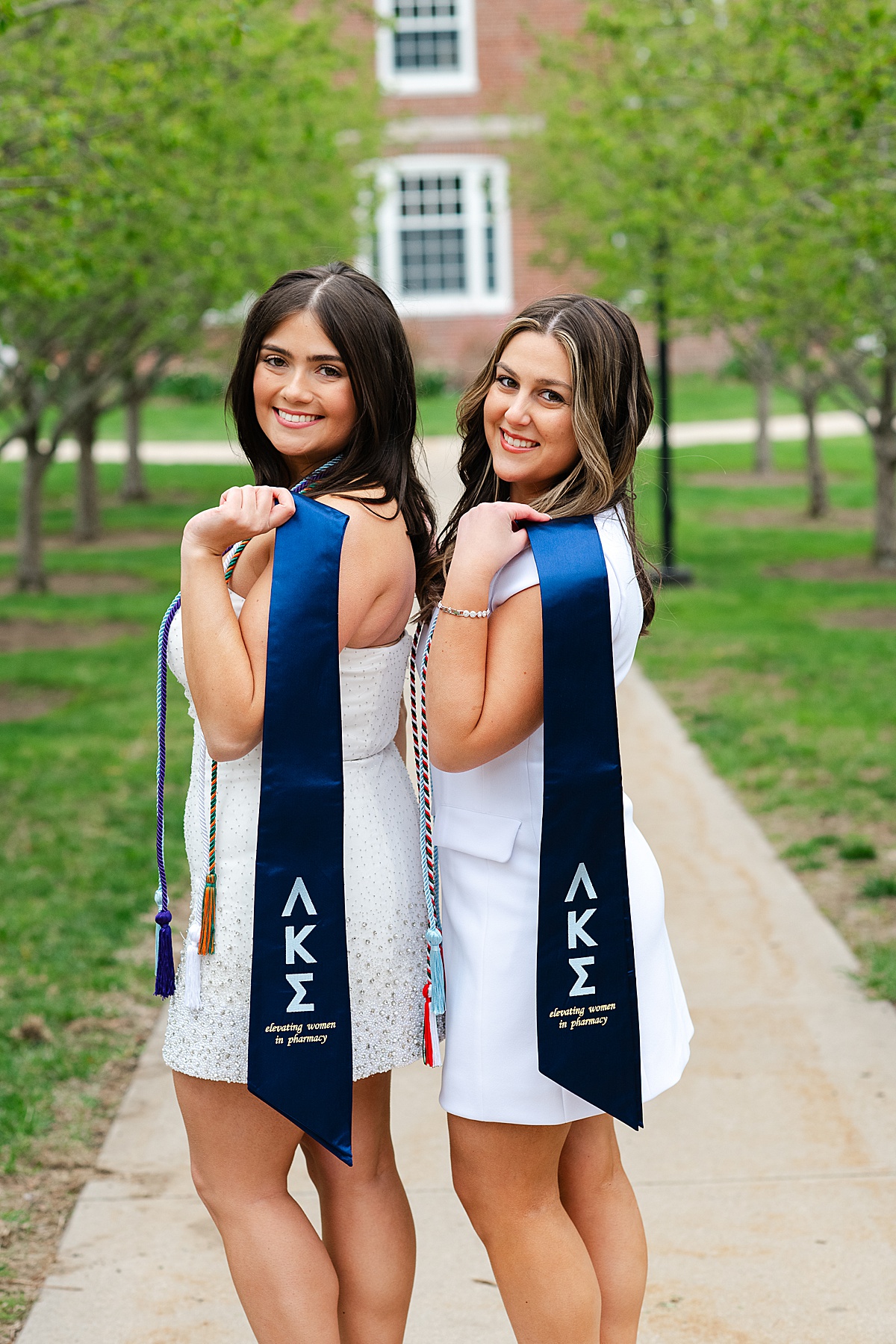 college graduates posing with sorority sashes beneath a row of trees