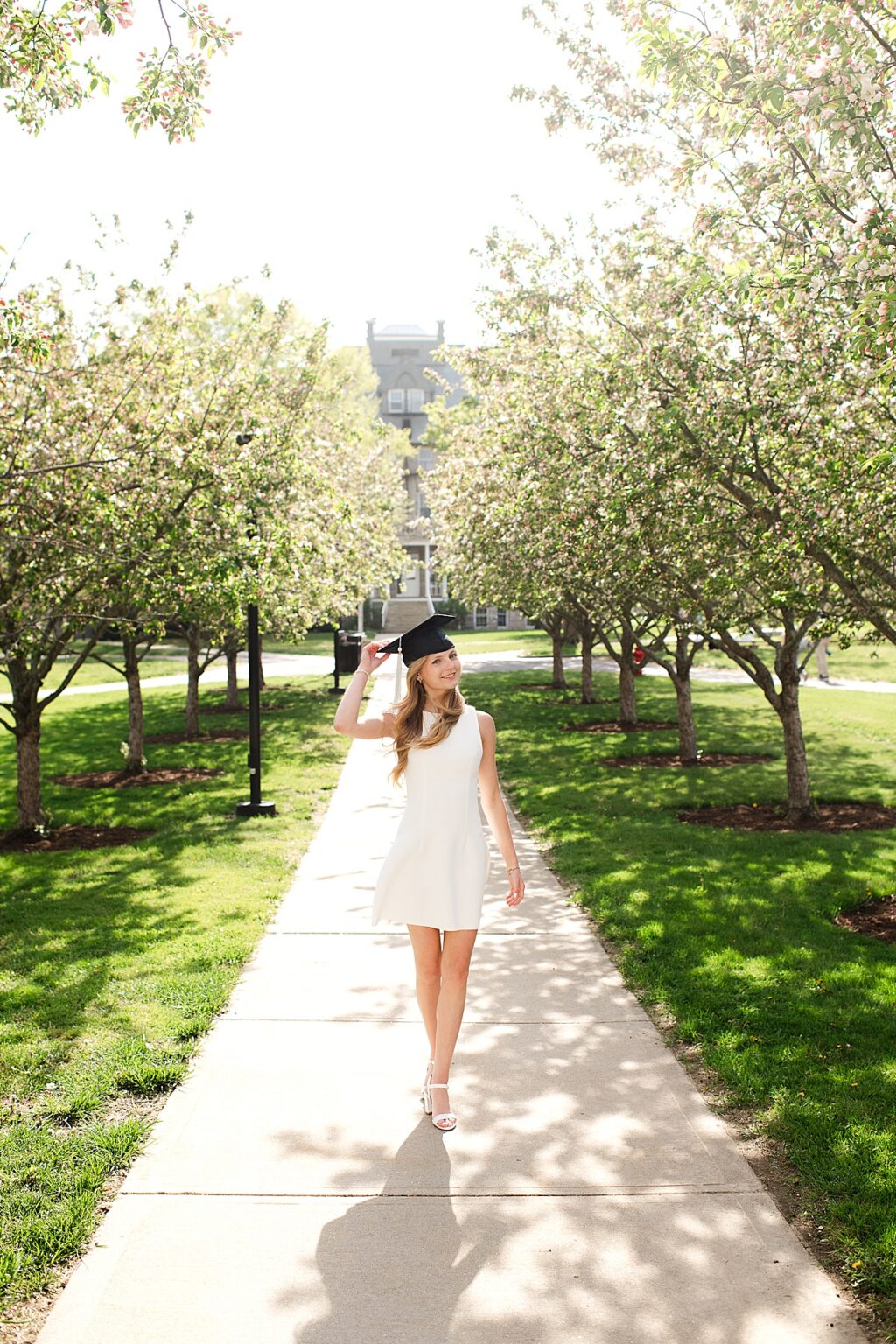 URI graduate walking through row of trees holding cap